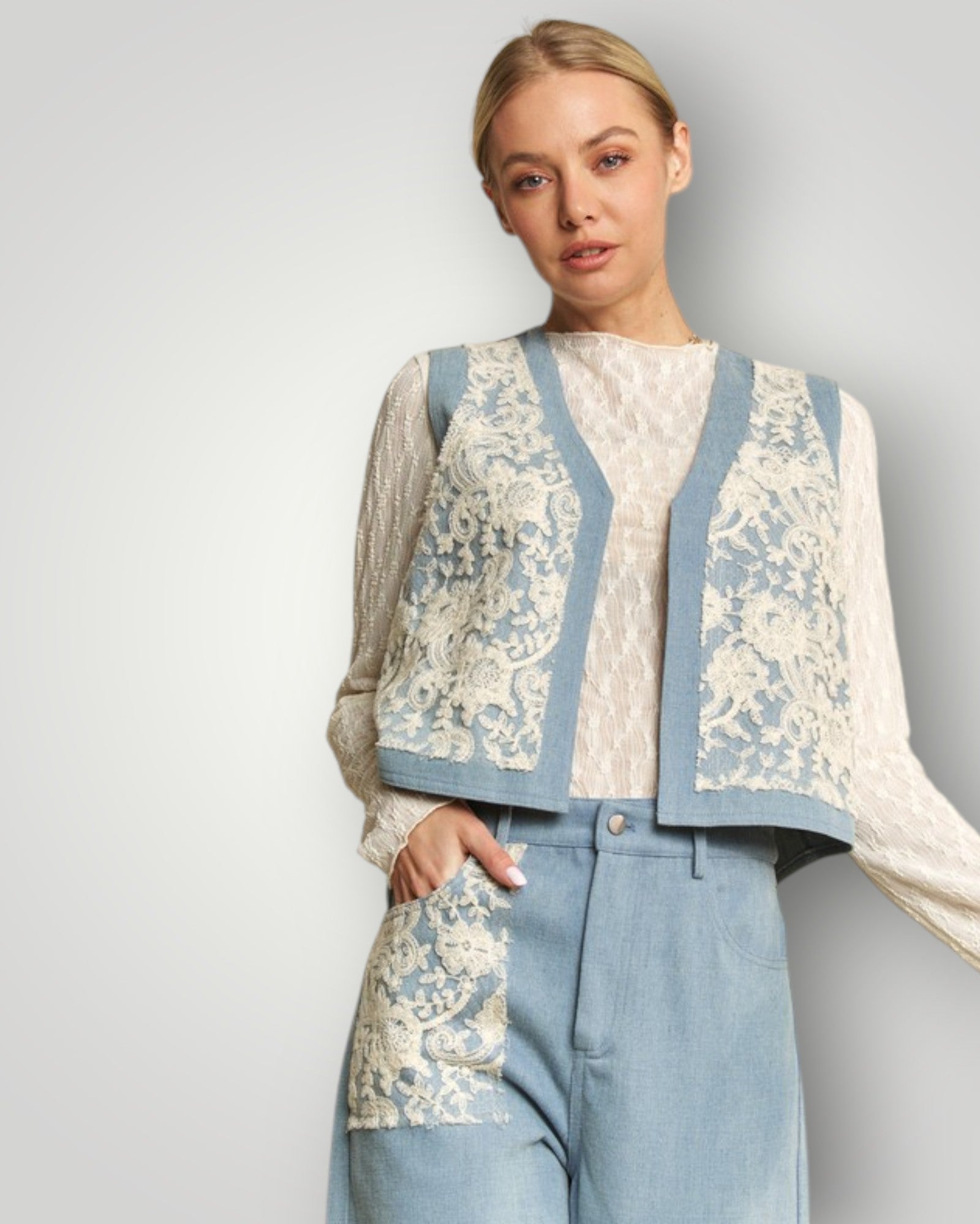 Woman wearing a floral-patterned cardigan over a white blouse with blue pants on a plain background