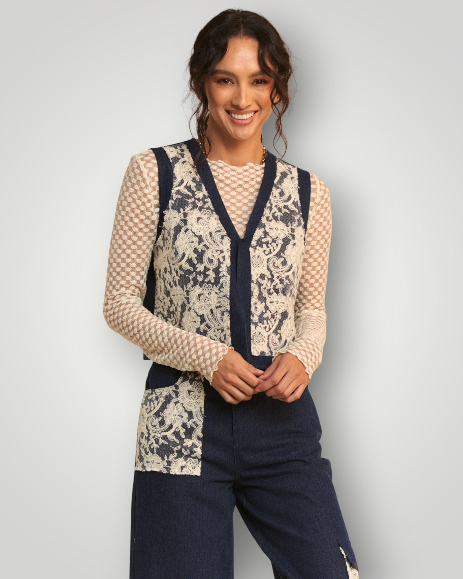Woman wearing a floral lace cardigan over a navy outfit on a light gray background