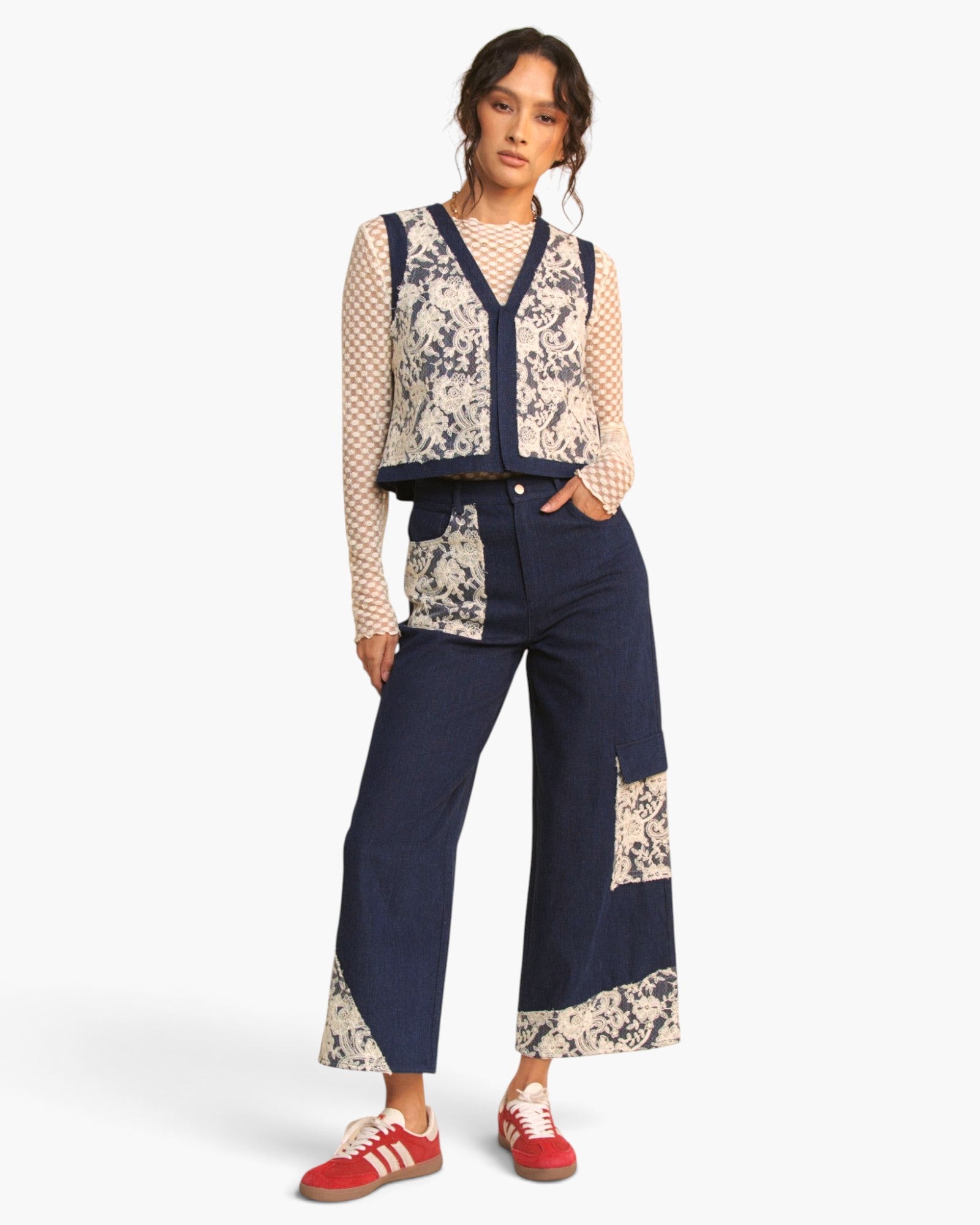 A model wearing a matching navy and beige patchwork vest and wide-leg cropped pants, styled with a beige patterned long-sleeve top and red sneakers, against a plain white studio background.