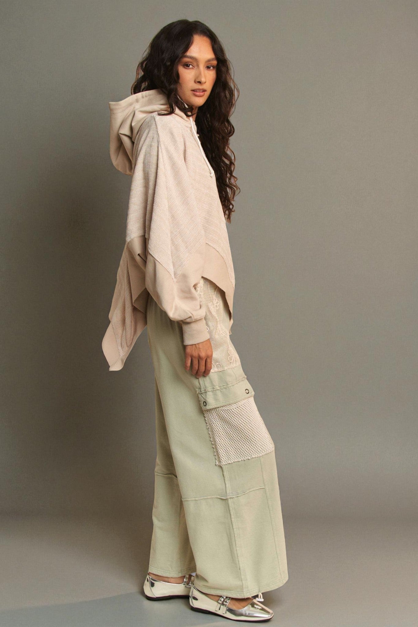 Woman wearing a beige oversized hoodie and light green cargo pants against a gray background