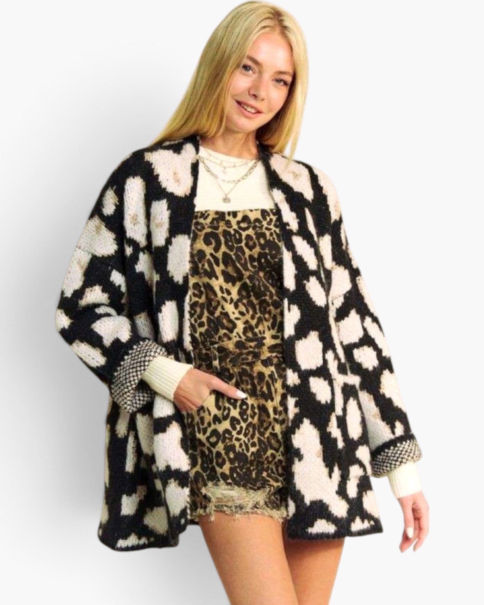 A woman modeling a black and cream ikat pattern open-front cardigan over a leopard-print dress, photographed against a light gray studio background.
