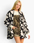 A woman modeling a black and cream ikat pattern open-front cardigan over a leopard-print dress, photographed against a light gray studio background.