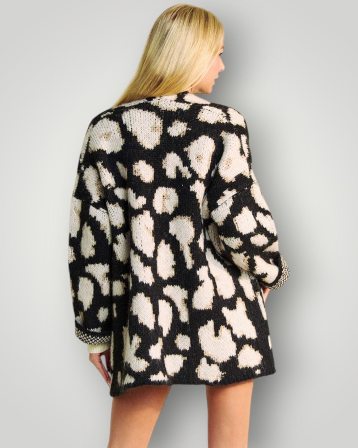 Person wearing a black and white patterned cardigan on a plain background