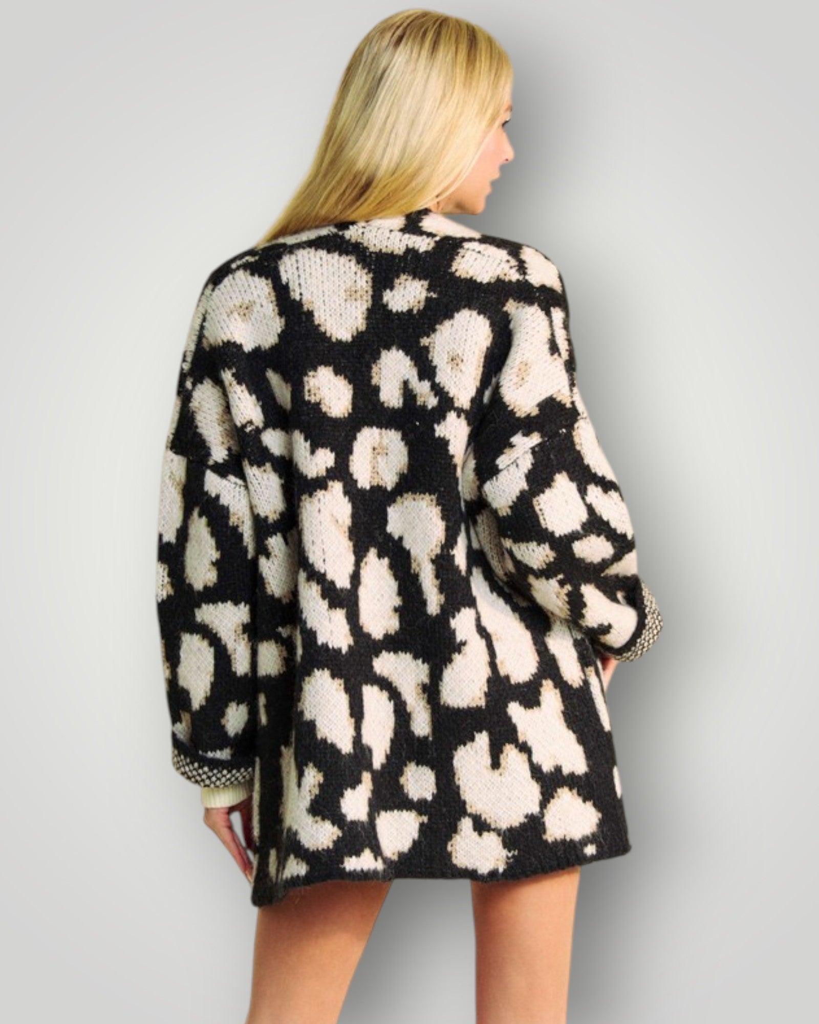 Person wearing a black and white patterned cardigan on a plain background