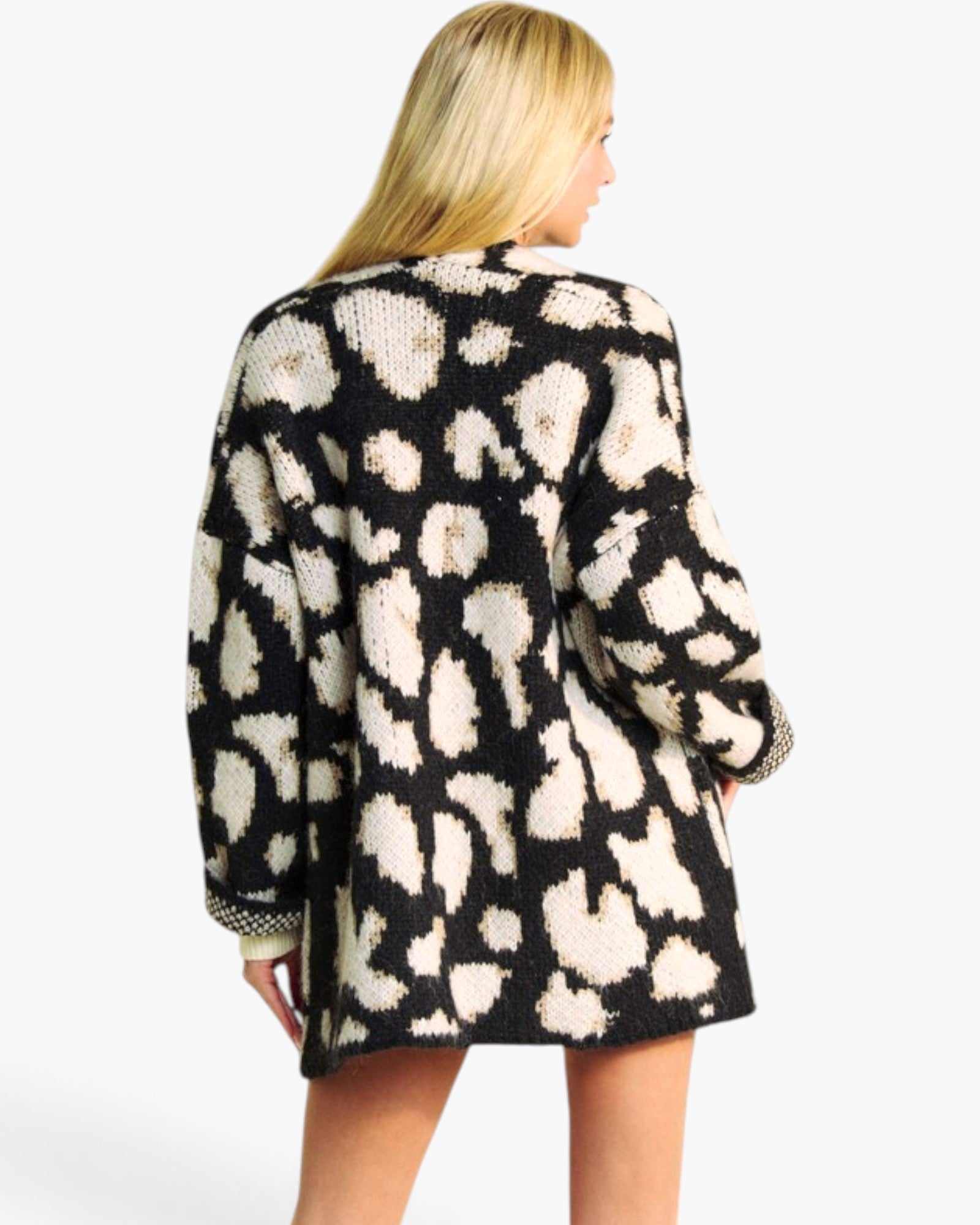 A woman shown from the back wearing a black knit cardigan with a large cream leopard print pattern, photographed against a plain light gray studio background.