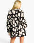 A woman shown from the back wearing a black knit cardigan with a large cream leopard print pattern, photographed against a plain light gray studio background.