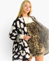 A woman modeling a black and white ikat pattern knit cardigan layered over a leopard print dress, against a plain white studio background.