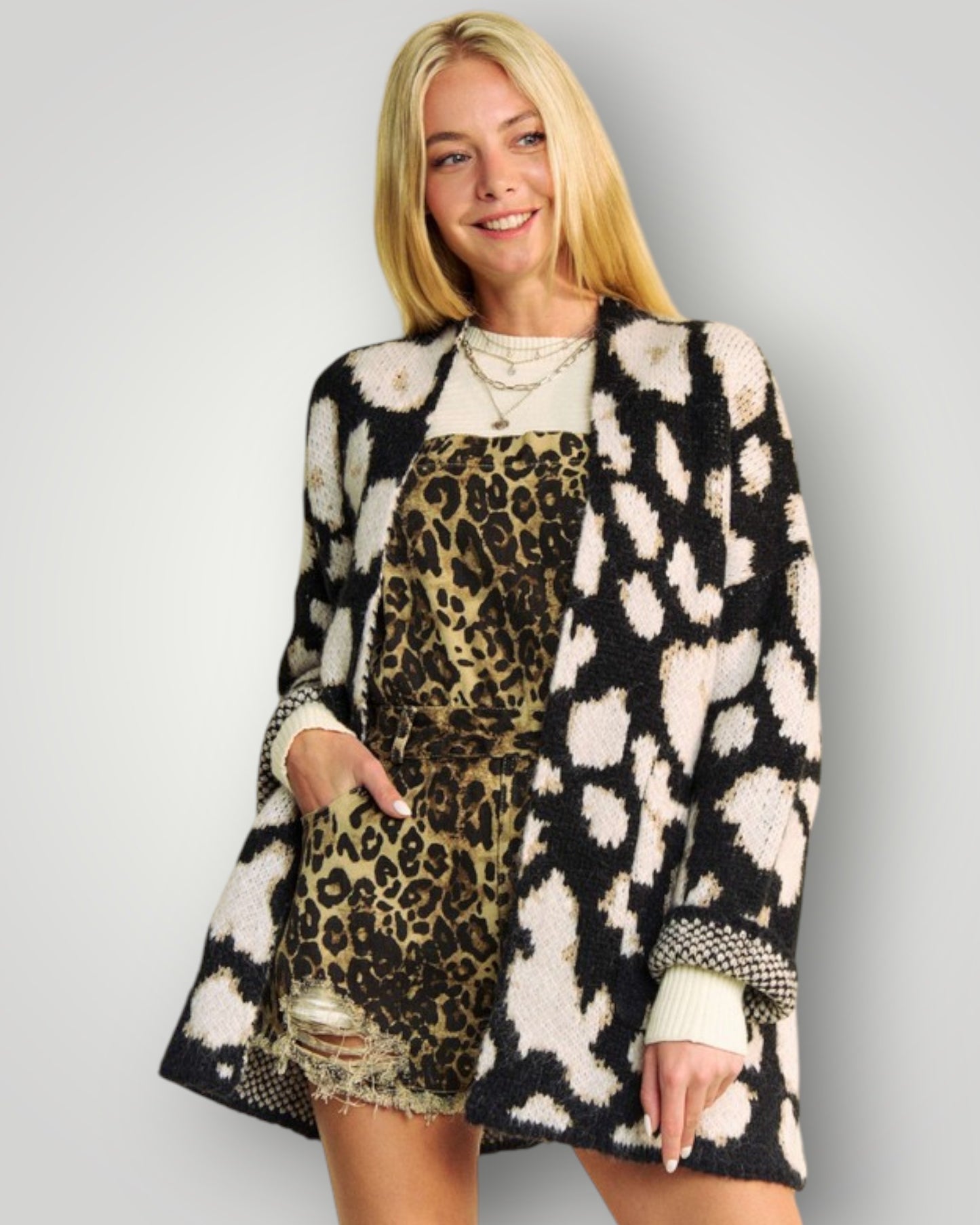 Woman wearing a patterned coat over a leopard print dress on a plain background