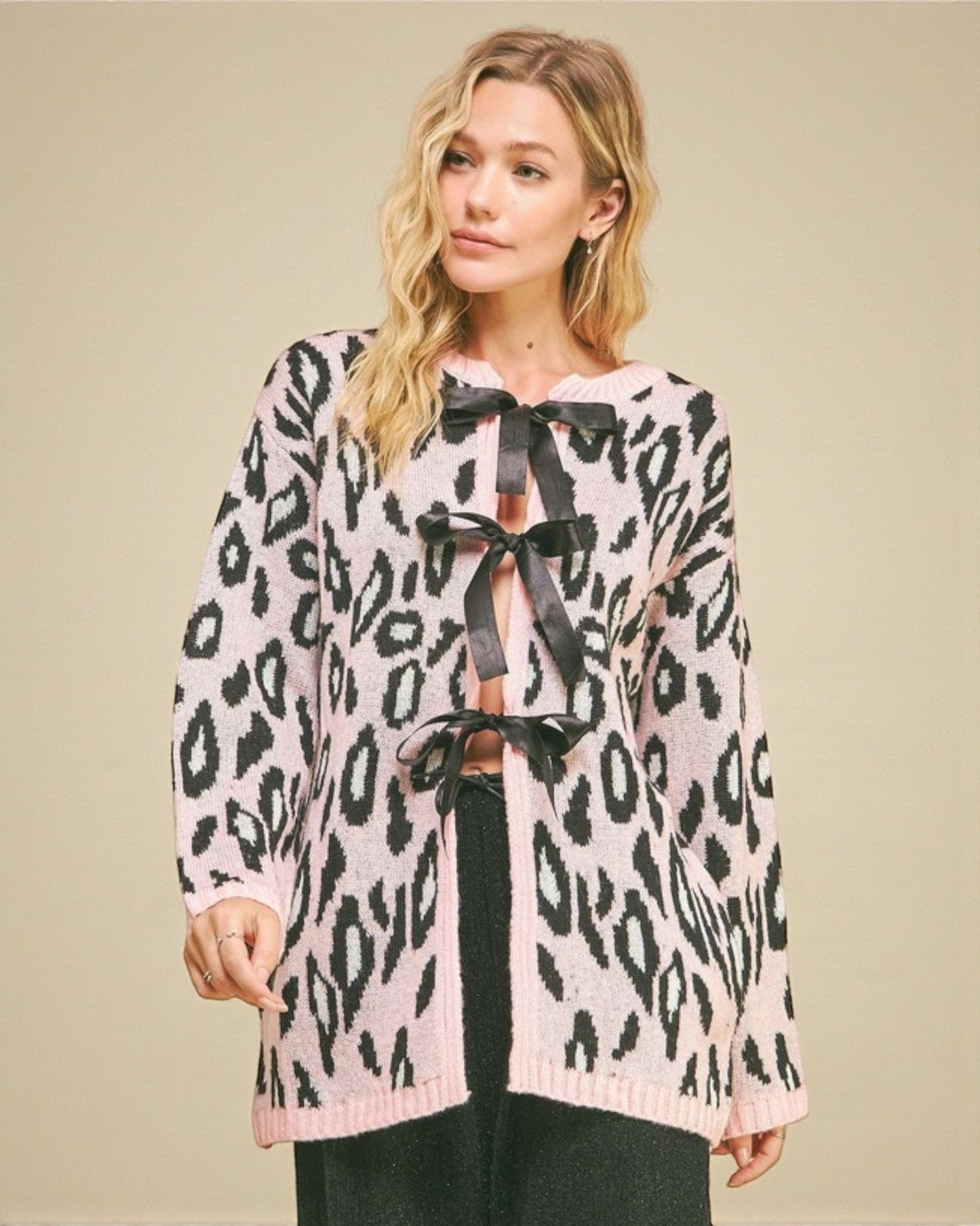 Woman wearing a leopard print cardigan with a black bow tie on a beige background