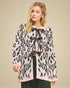 Woman wearing a leopard print cardigan with a black bow tie on a beige background