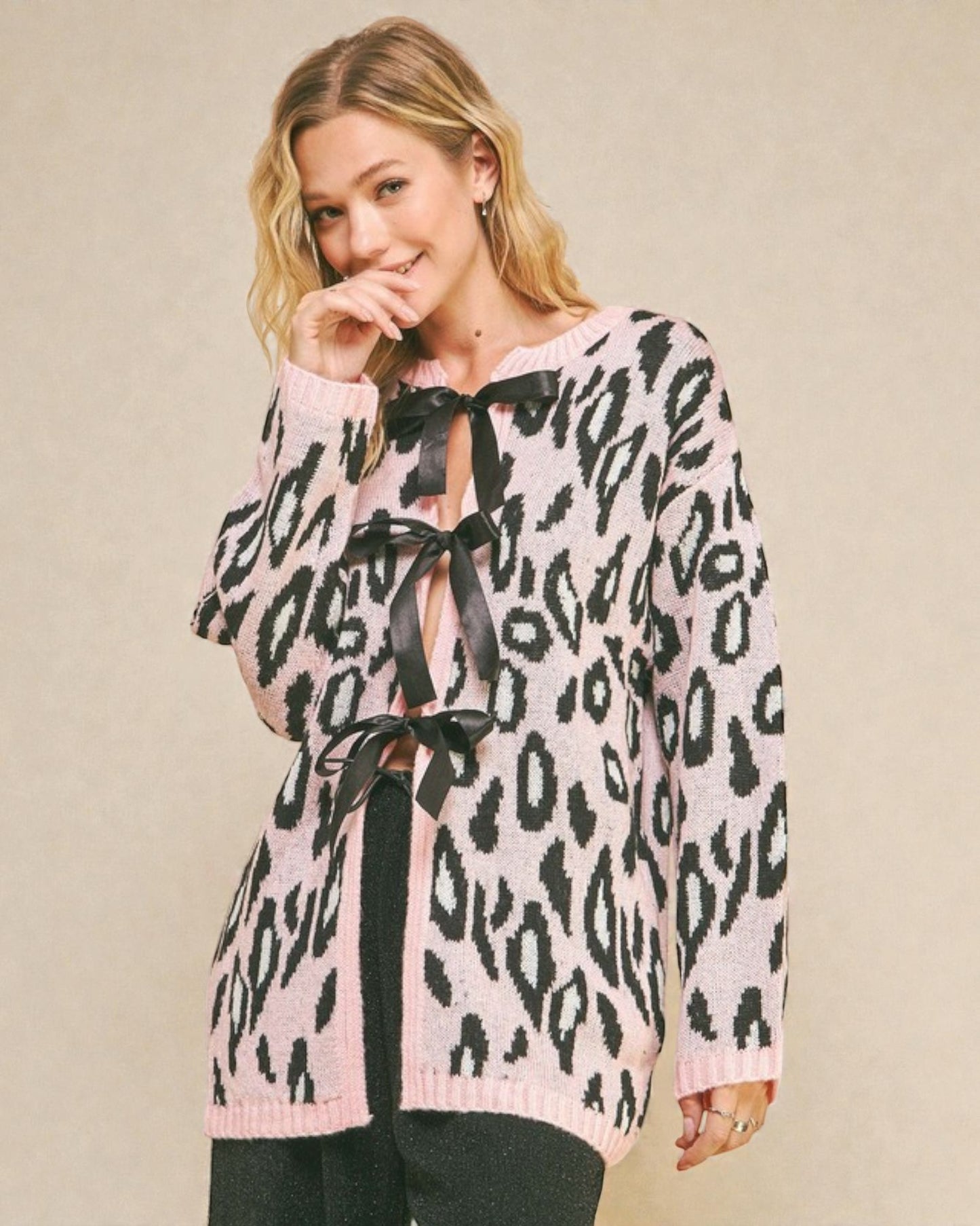 Woman wearing a pink leopard print blouse with black ribbons on a beige background