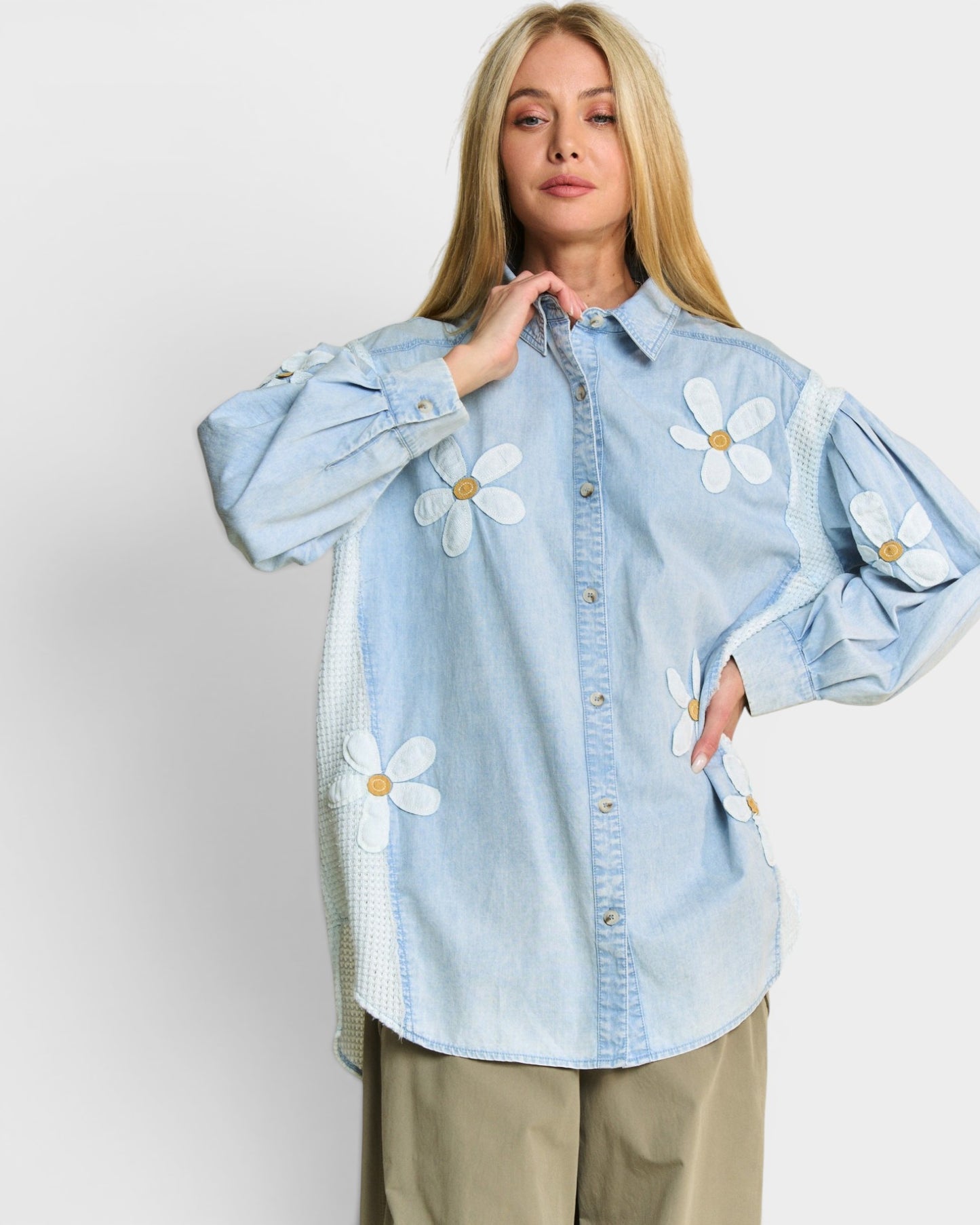 Woman wearing a light blue denim shirt with white floral patches on a plain background