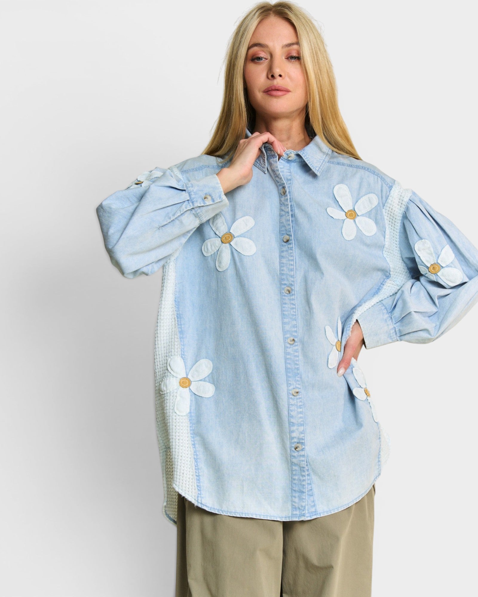 Woman wearing a light blue denim shirt with white floral patches on a plain background