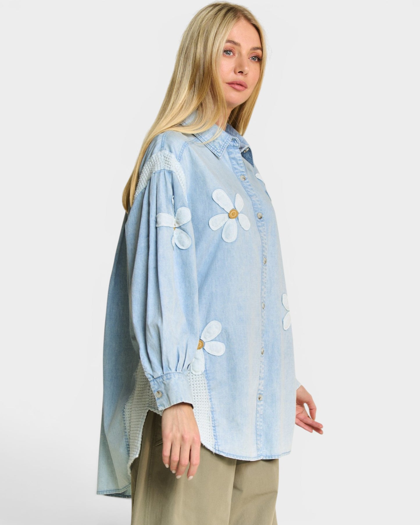 Woman wearing a light blue denim shirt with white floral patterns on a plain background