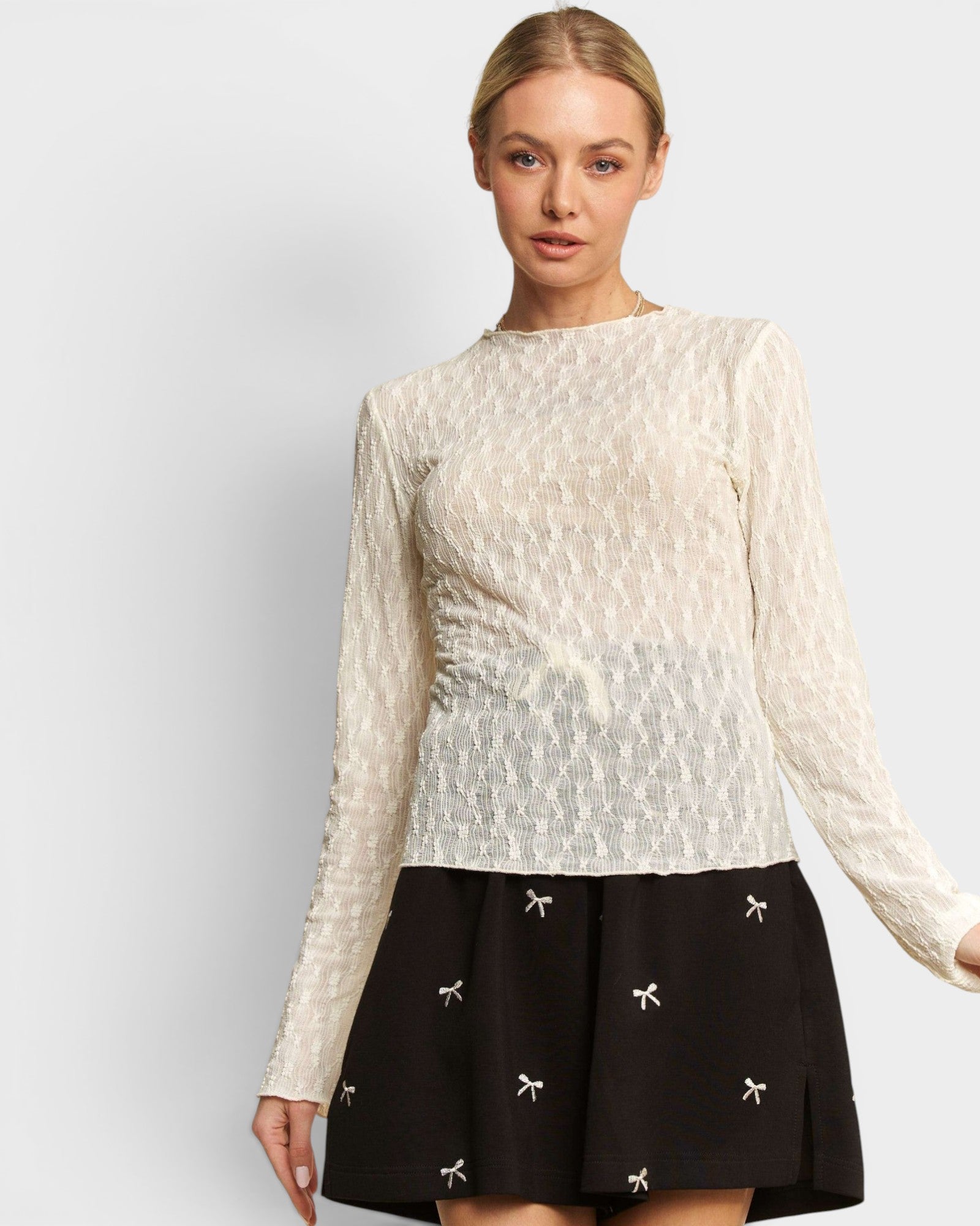 Woman wearing a white long-sleeve top and black skirt with white patterns on a light gray background