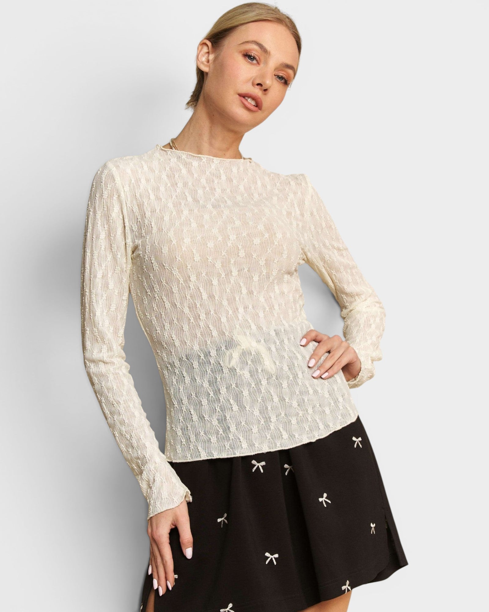 Woman wearing a white lace top and black skirt with white patterns on a light gray background