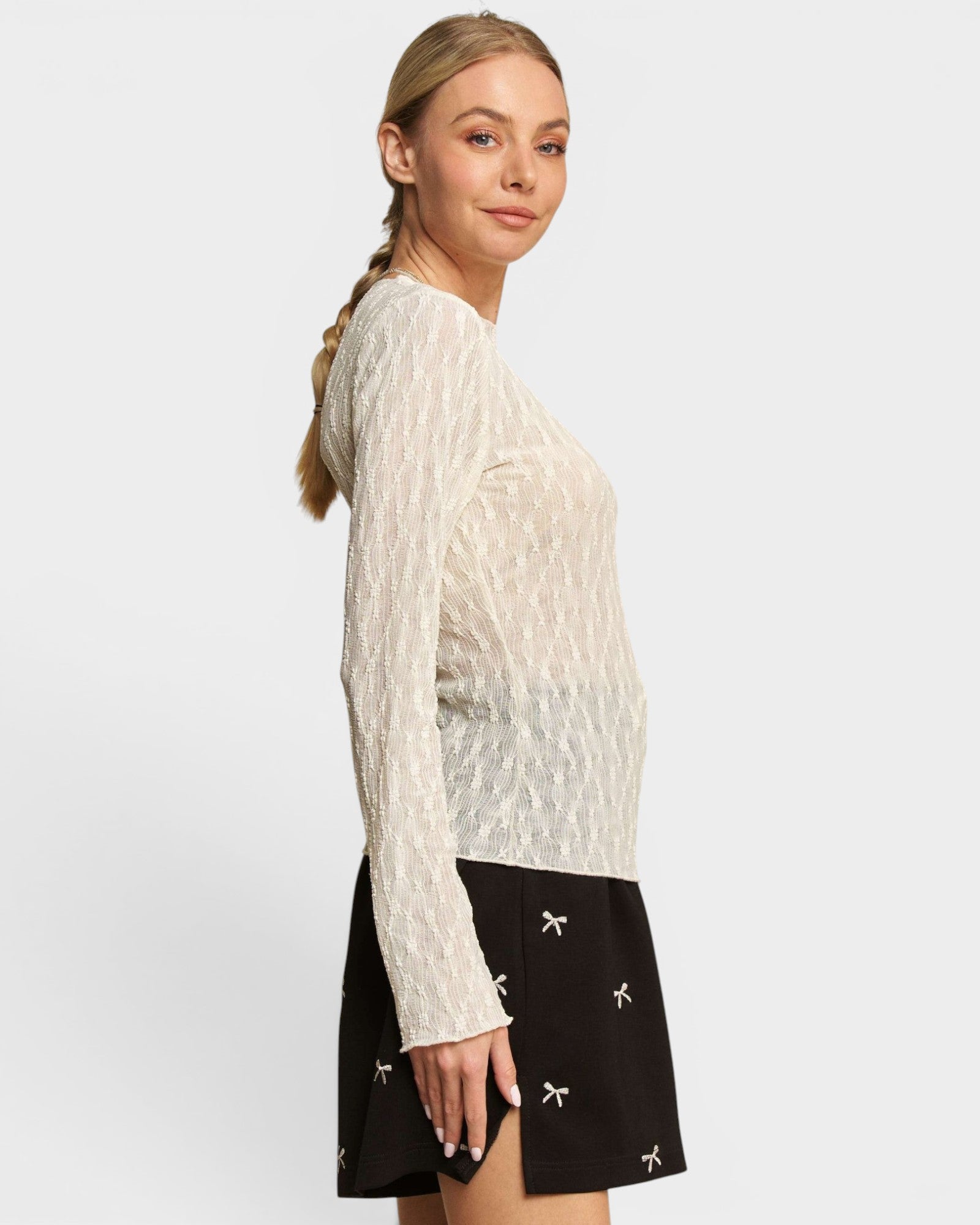 Woman wearing a white cable knit sweater and black skirt with white patterns on a light gray background