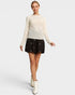 Woman wearing a cream sweater and black skirt with white booties on a light gray background
