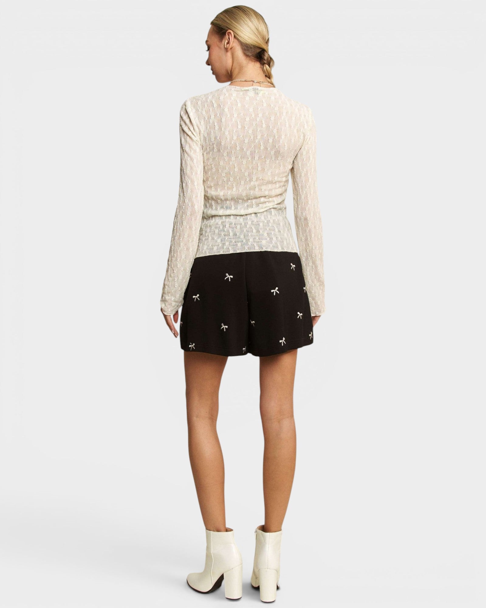 Woman wearing a white long-sleeve top and black shorts with white patterns on a white background
