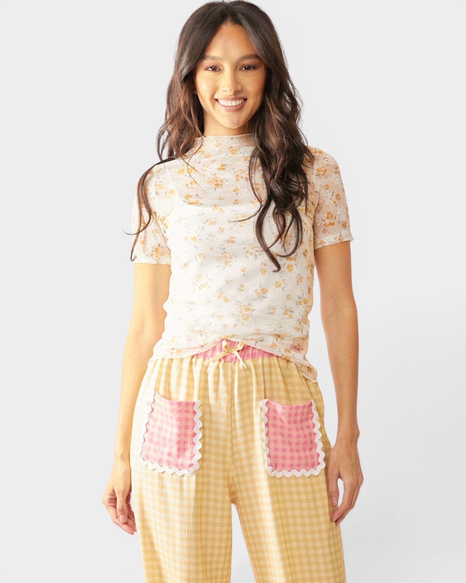Woman wearing a floral top and checkered pants with pink accents on a white background