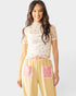 Woman wearing a floral top and checkered pants with pink accents on a white background