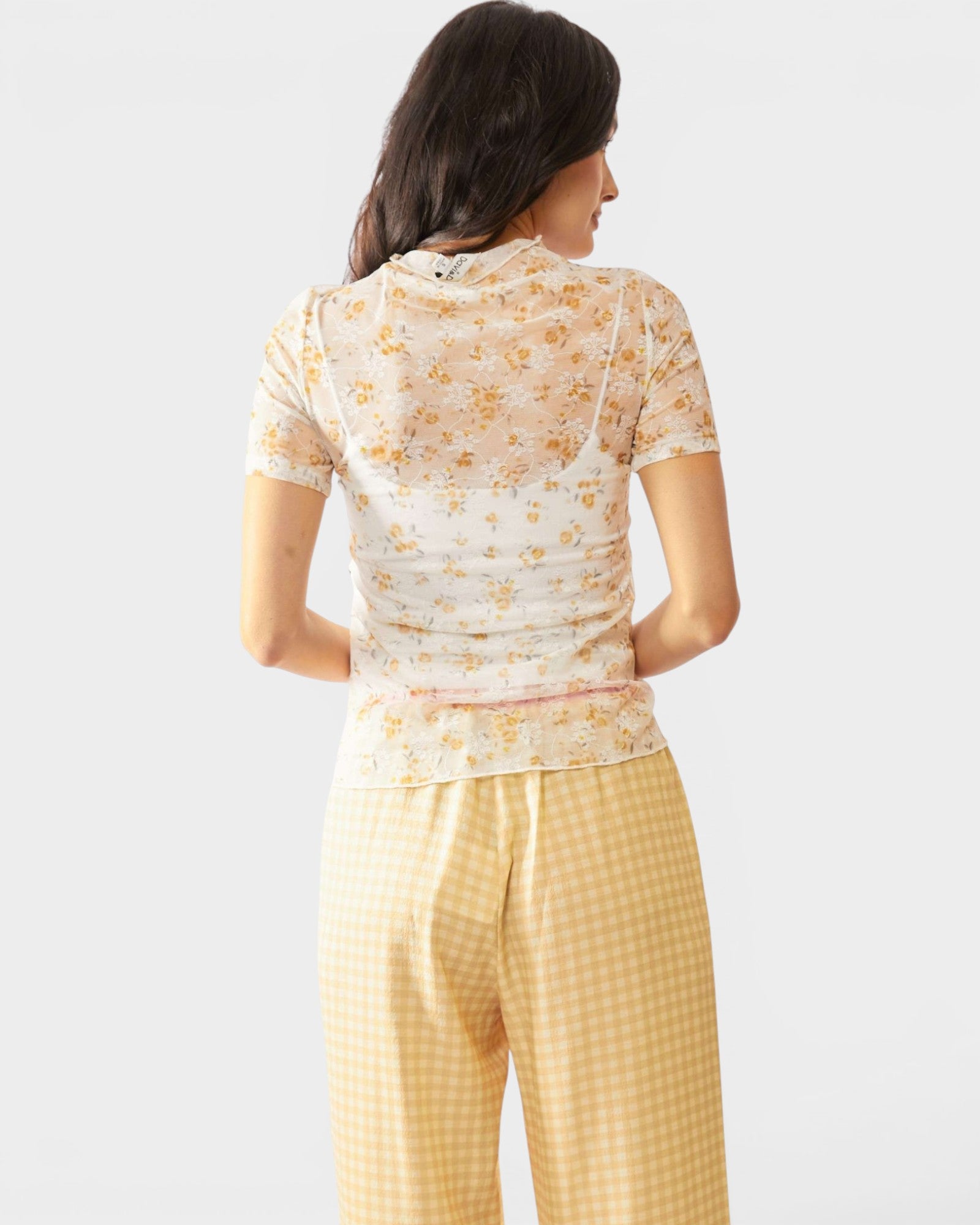 Woman wearing a floral top and yellow checkered pants on a white background