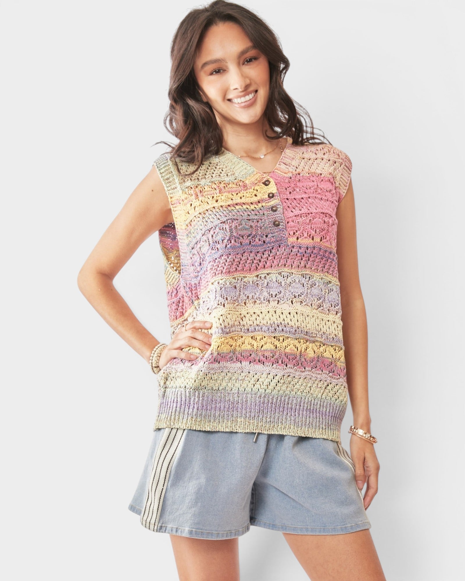 Woman wearing a colorful crochet sleeveless top with denim shorts on a white background