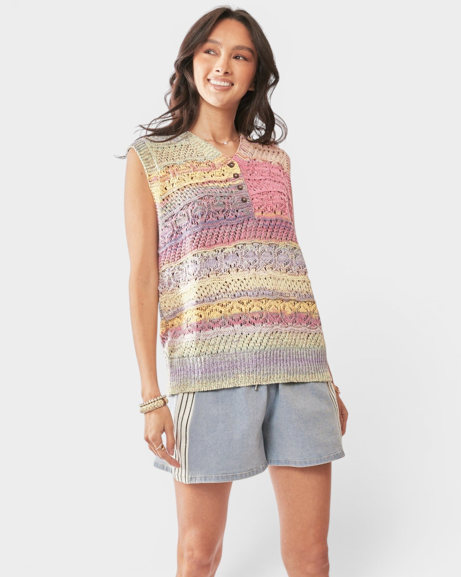 Woman wearing a colorful sleeveless crochet top and denim shorts on a white background