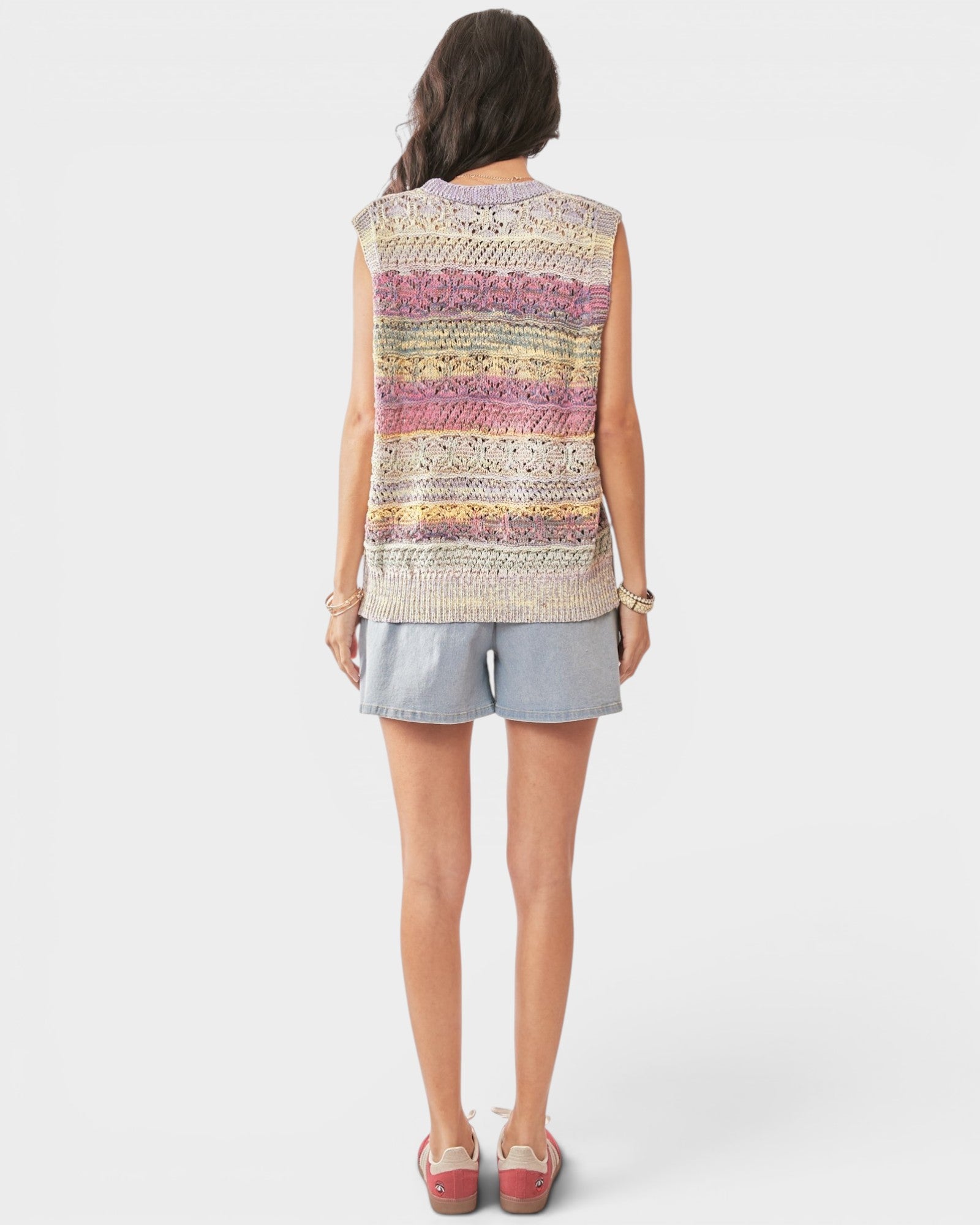 Woman wearing a sleeveless, multicolored knit top and light blue shorts on a white background
