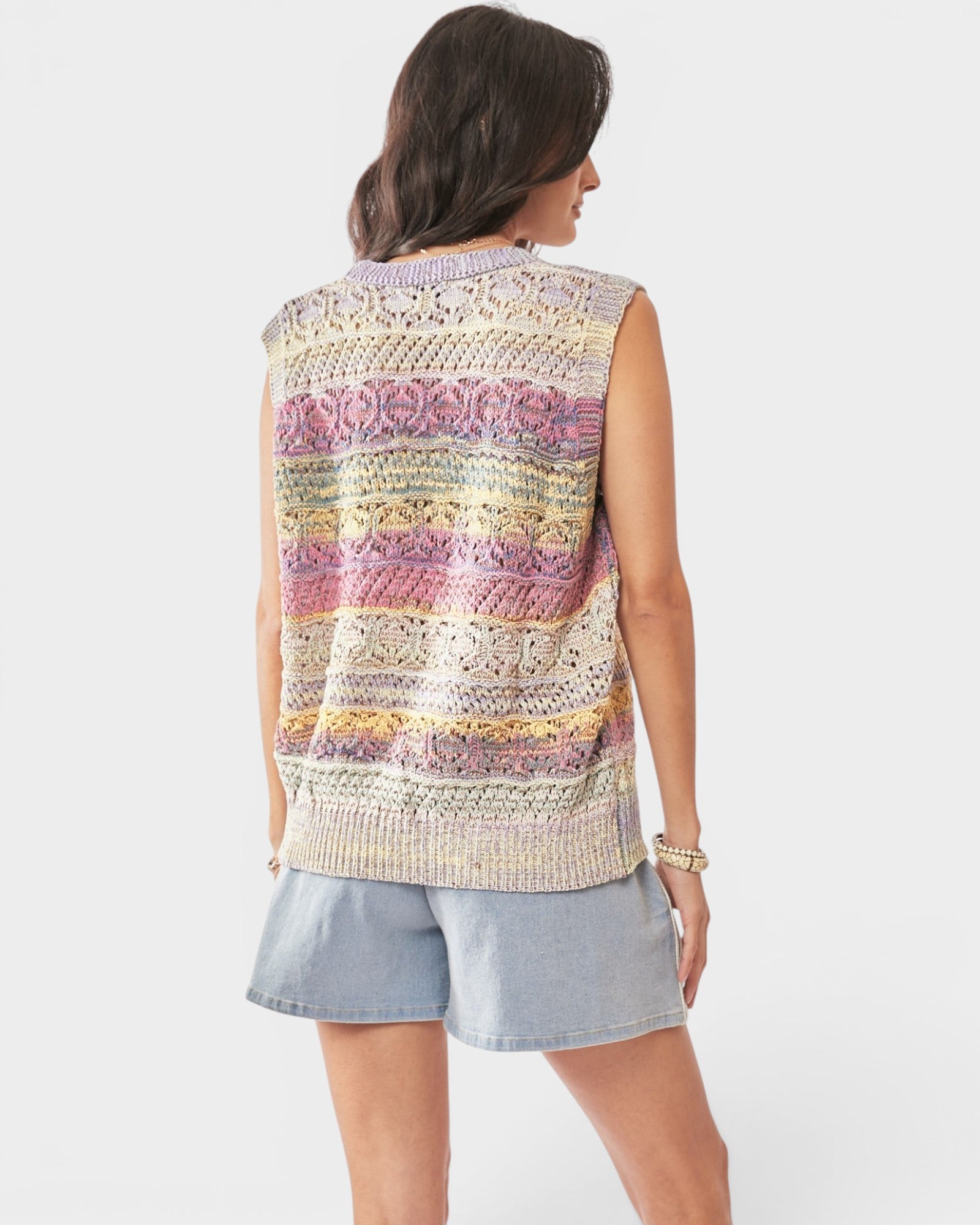 Woman wearing a colorful sleeveless crochet top and denim shorts on a white background