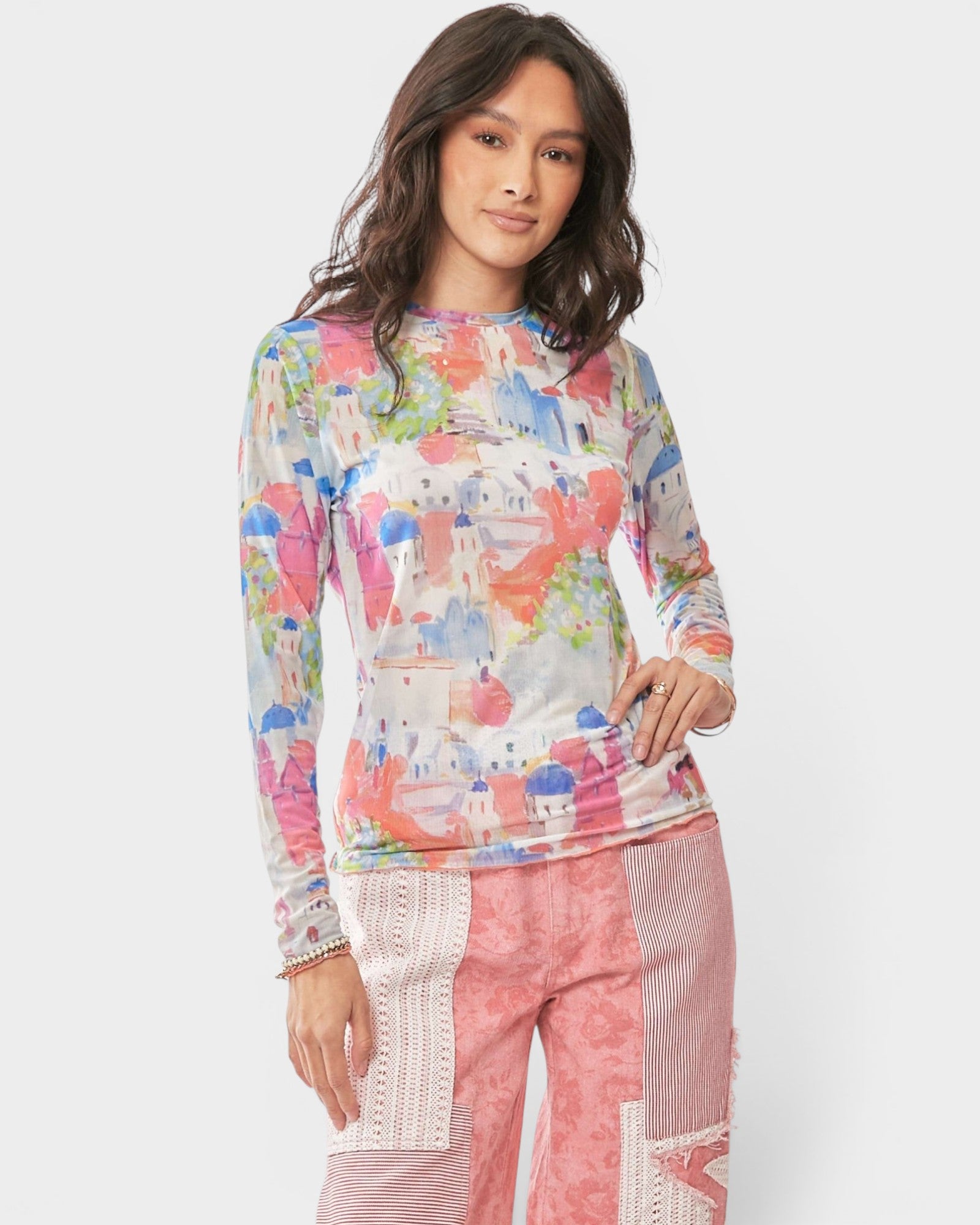 Woman wearing a colorful long-sleeve top and pink pants on a white background