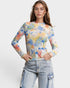 Woman wearing a colorful long-sleeve top with a pattern of buildings and blue jeans on a white background