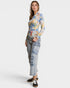 Woman wearing a colorful long-sleeve top and light blue cargo pants on a white background