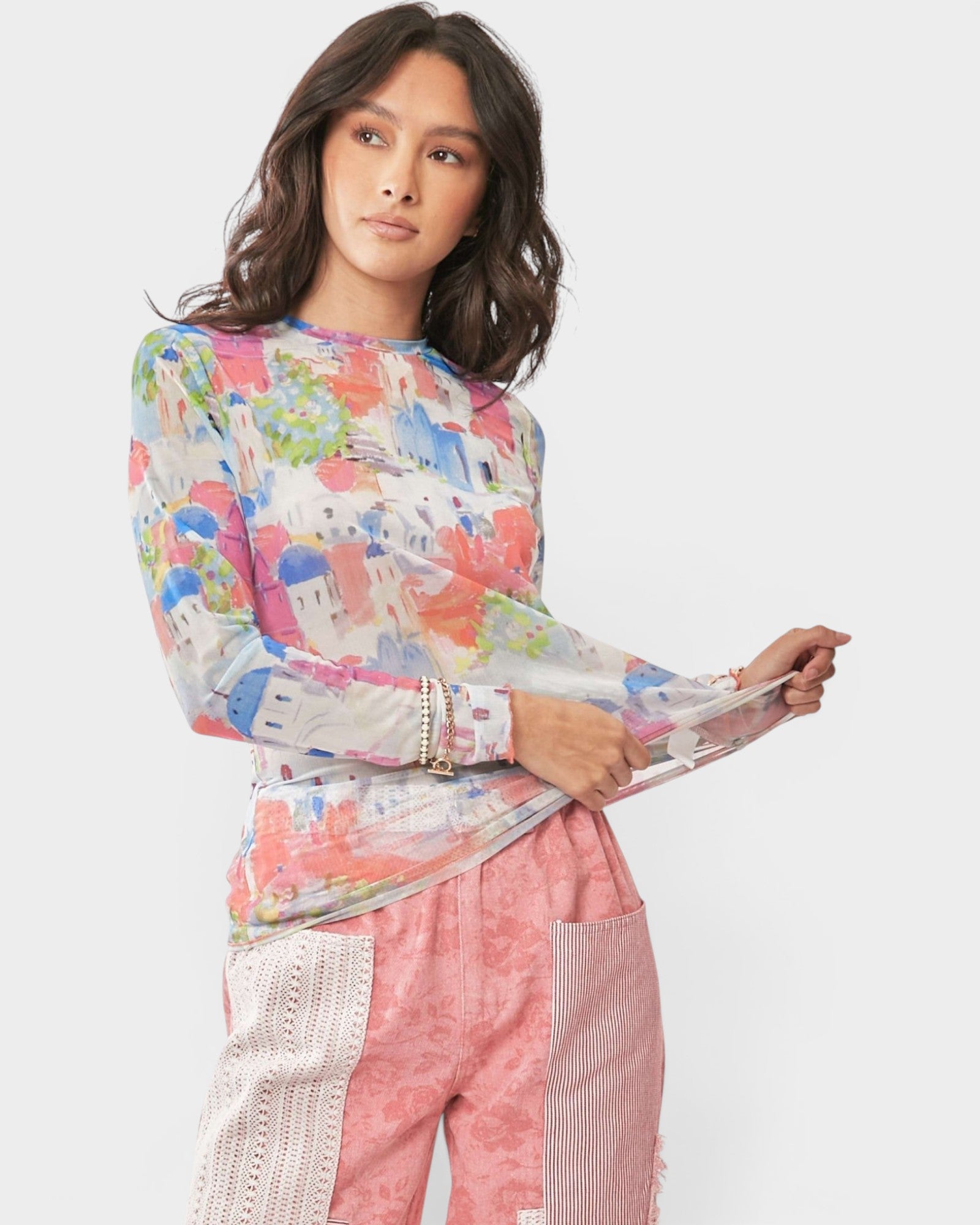 Woman wearing a colorful patterned top and pink pants on a white background