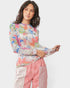 Woman wearing a colorful patterned top and pink pants on a white background