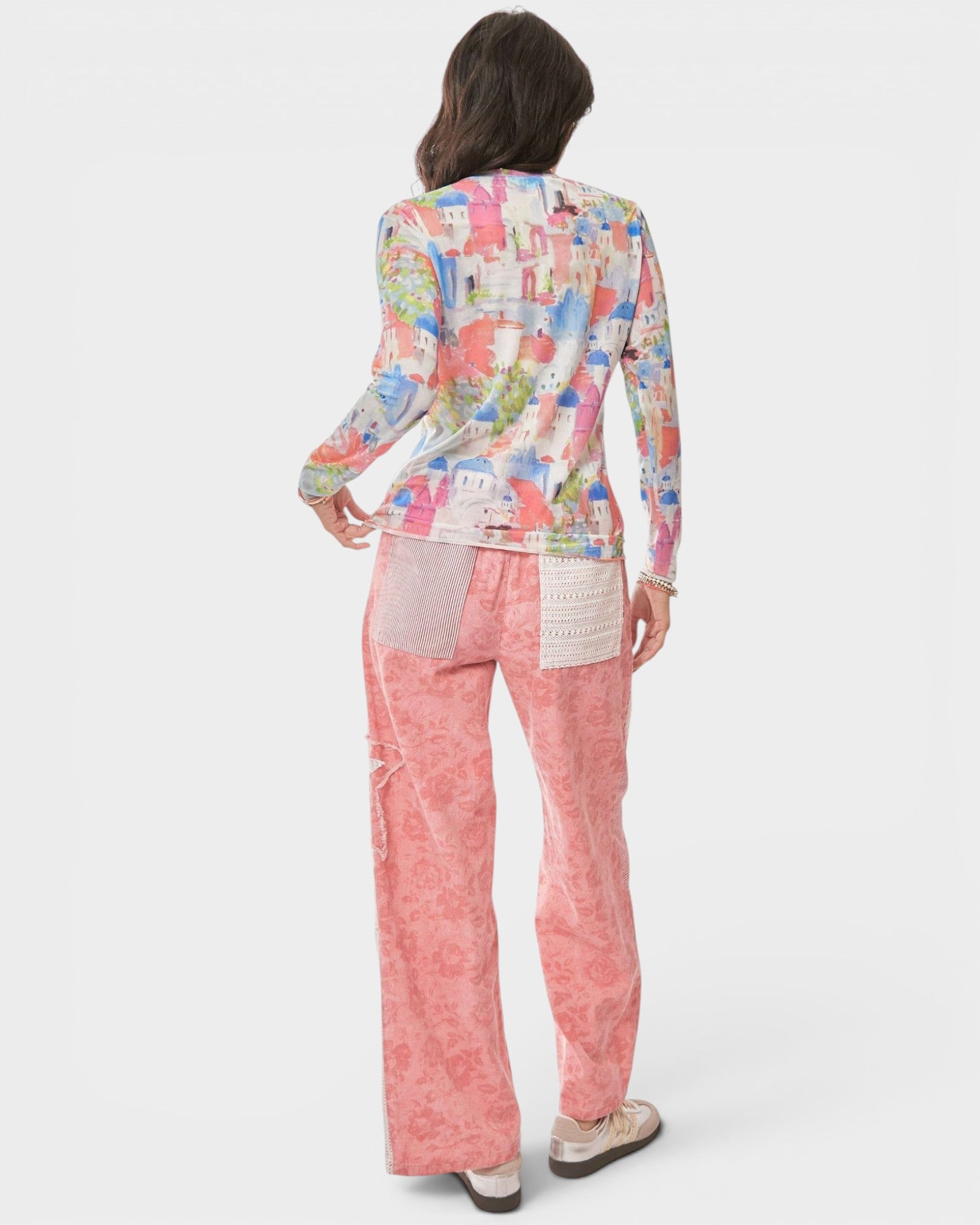 Woman wearing a colorful patterned jacket and pink pants on a white background