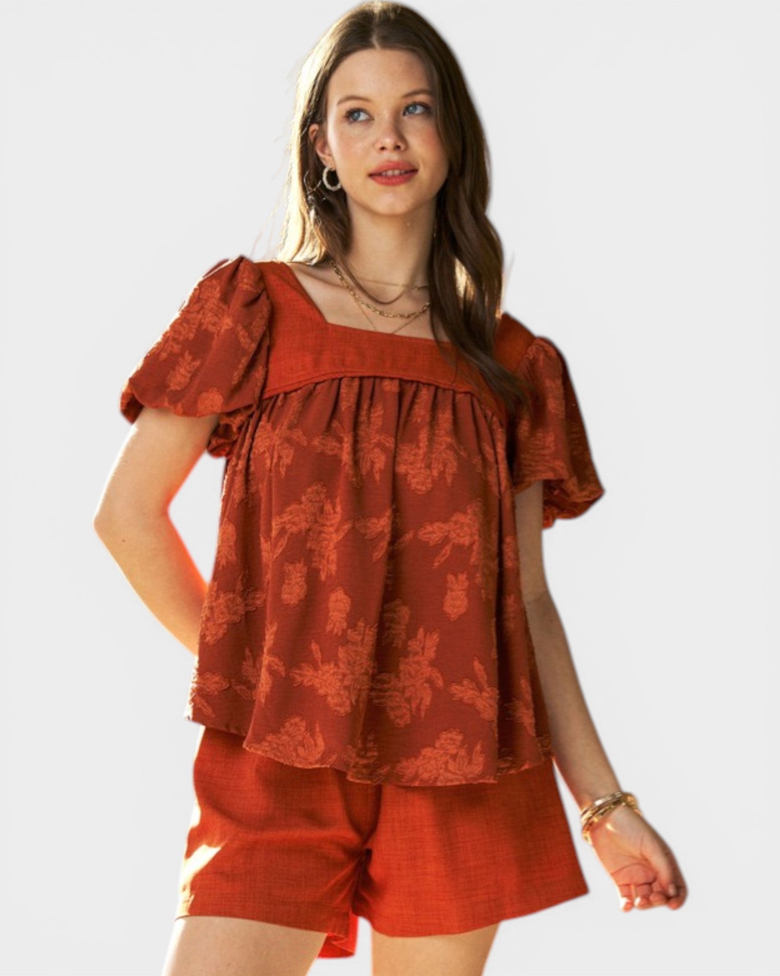 Woman wearing a rust-colored top and shorts on a white background