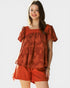 Woman wearing a red patterned top and shorts on a white background