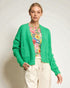 Woman wearing a green cardigan over a floral shirt with white pants on a plain background