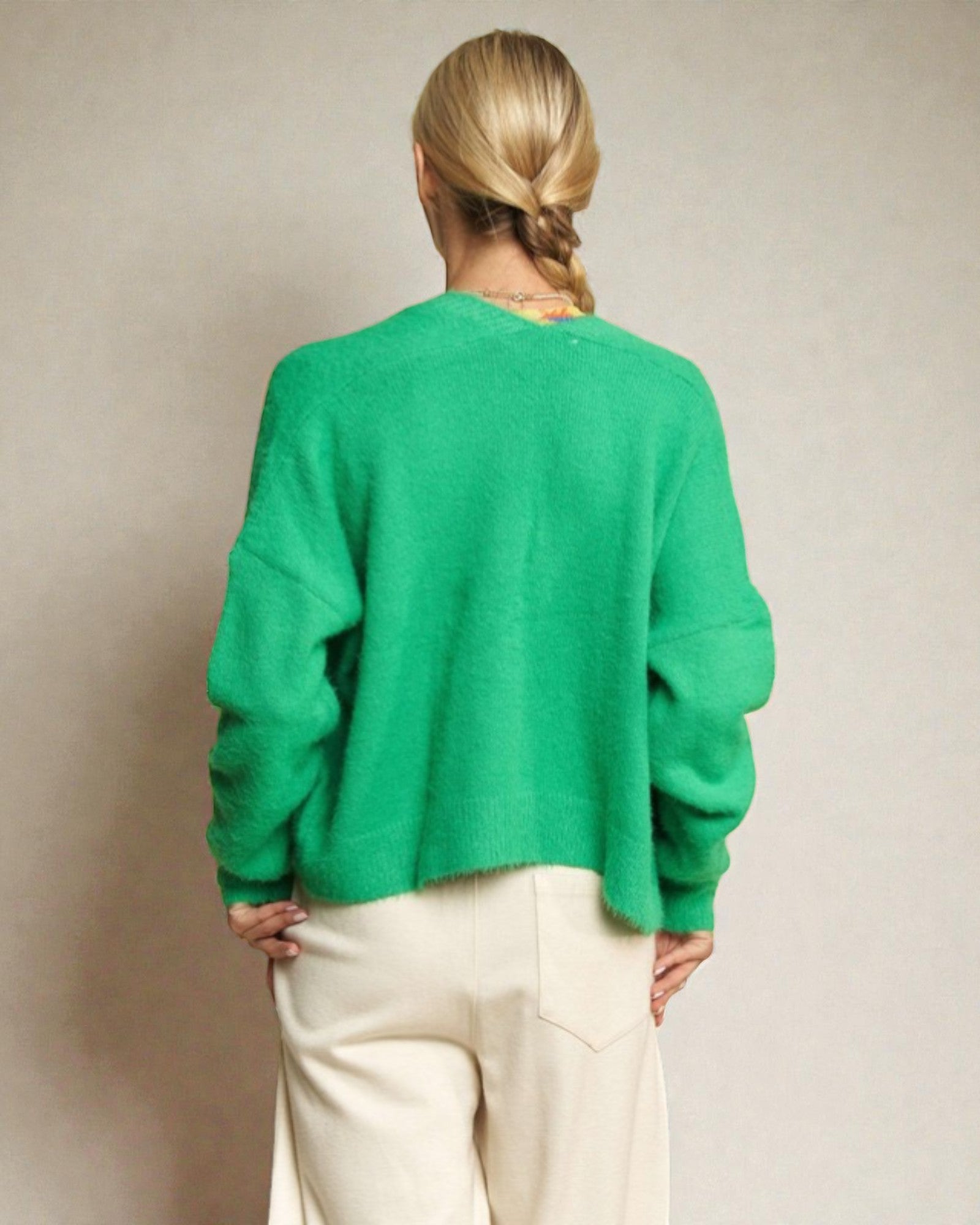 Person wearing a green sweater and white pants against a plain background