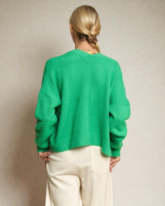Person wearing a green sweater and white pants against a plain background