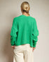 Person wearing a green sweater and white pants against a plain background