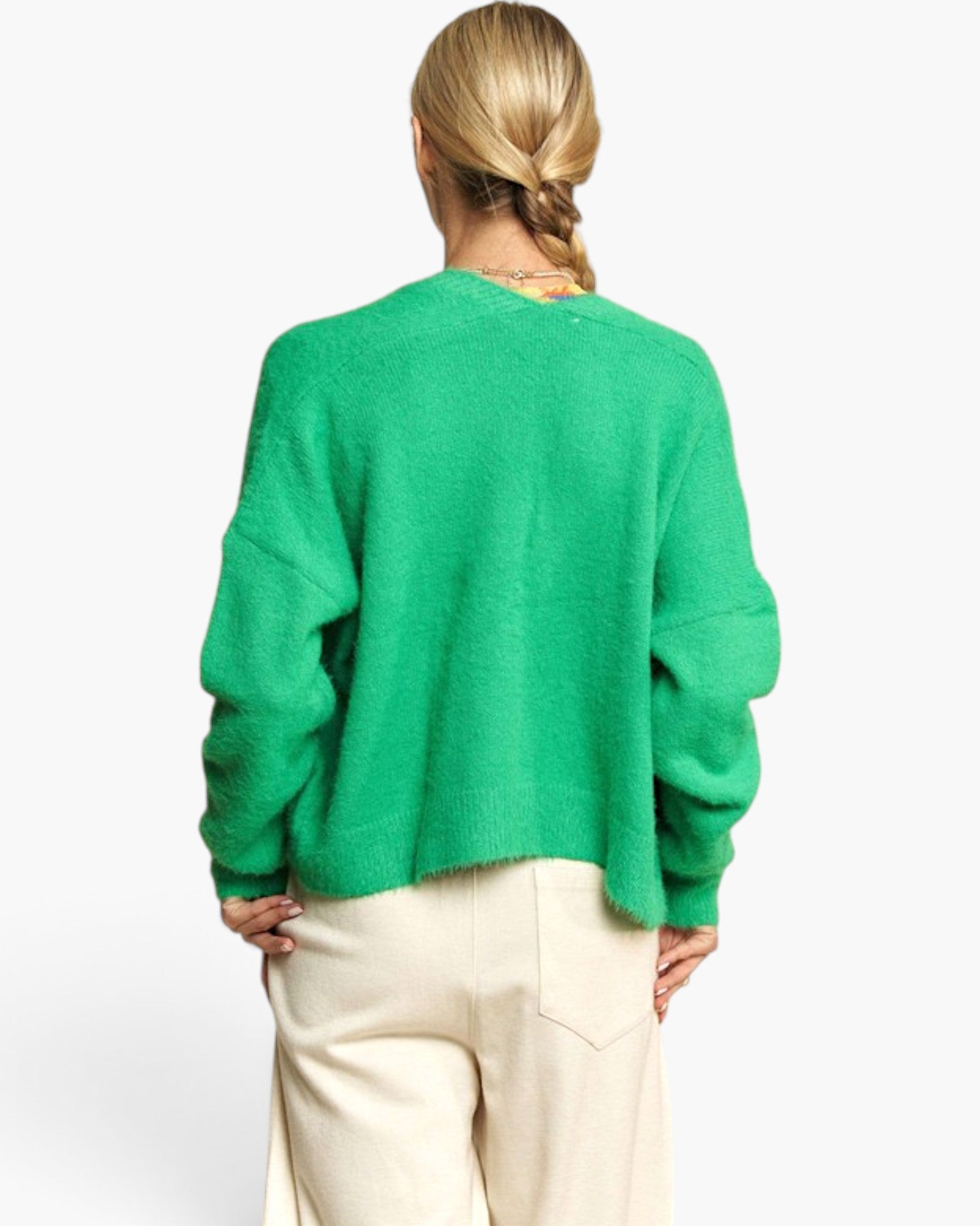 A woman viewed from behind wearing a fuzzy bright green cropped sweater and cream-colored pants, set against a plain white studio background.