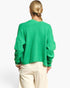 A woman viewed from behind wearing a fuzzy bright green cropped sweater and cream-colored pants, set against a plain white studio background.