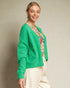Woman wearing a green cardigan over a floral shirt with a neutral background