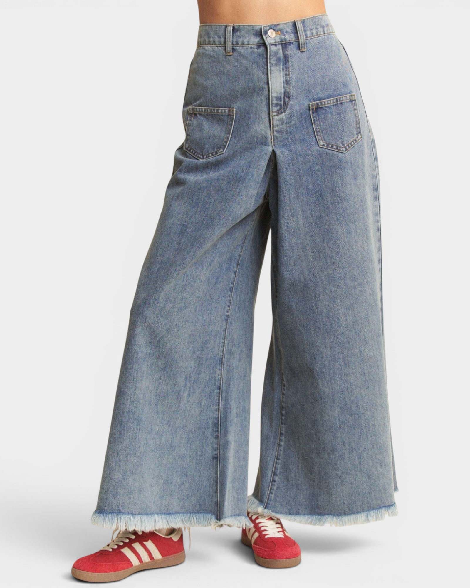 Wide-leg jeans worn with red sneakers on a white background
