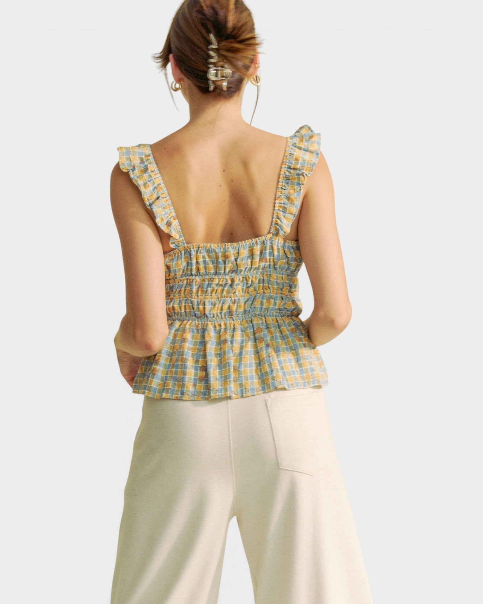 Woman wearing a yellow plaid top and white pants on a light gray background