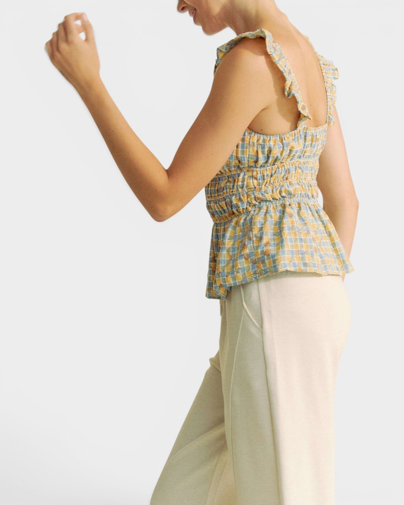 Woman wearing a yellow and blue checkered top with beige pants on a white background