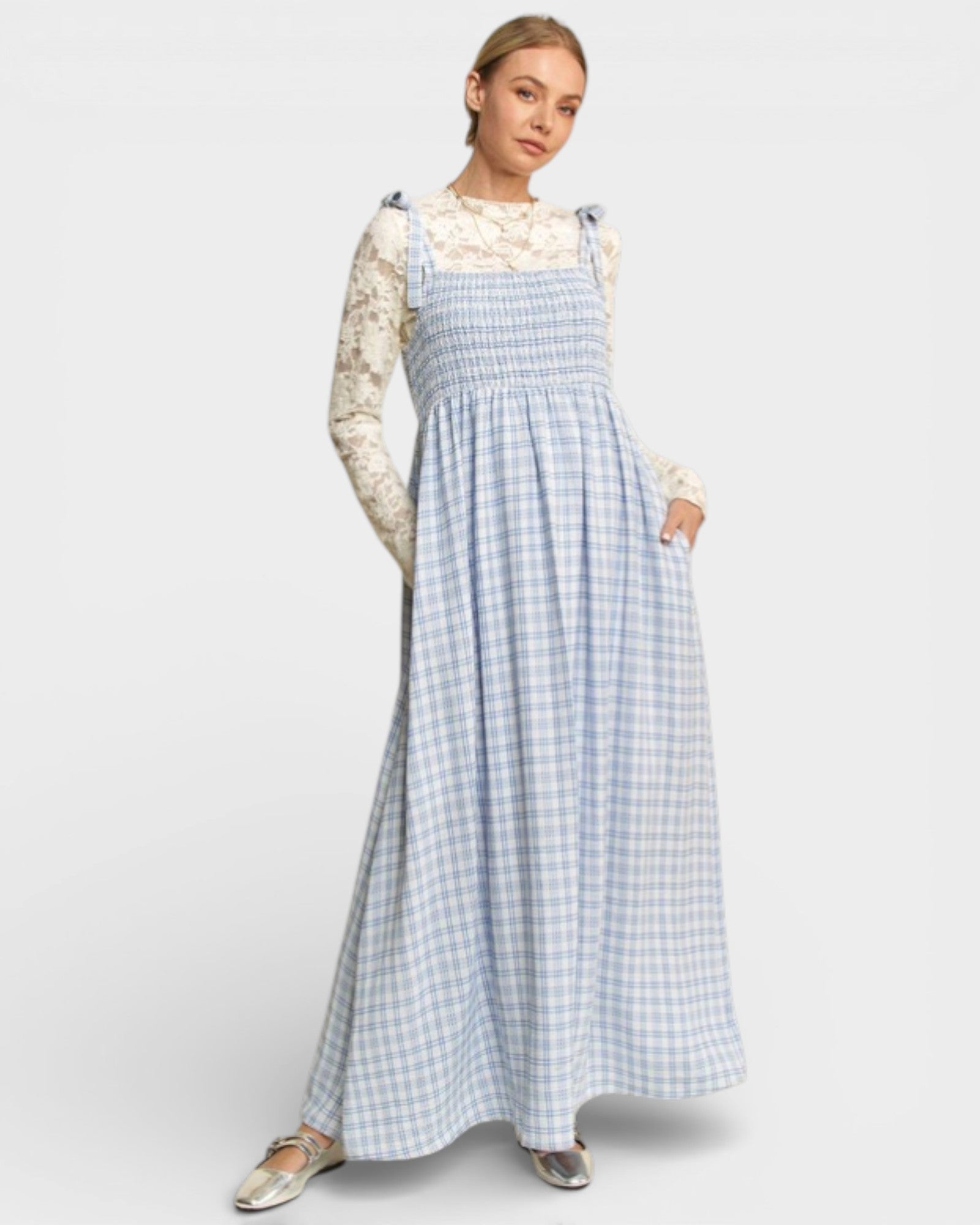 Woman wearing a blue checkered dress over a white lace top on a white background