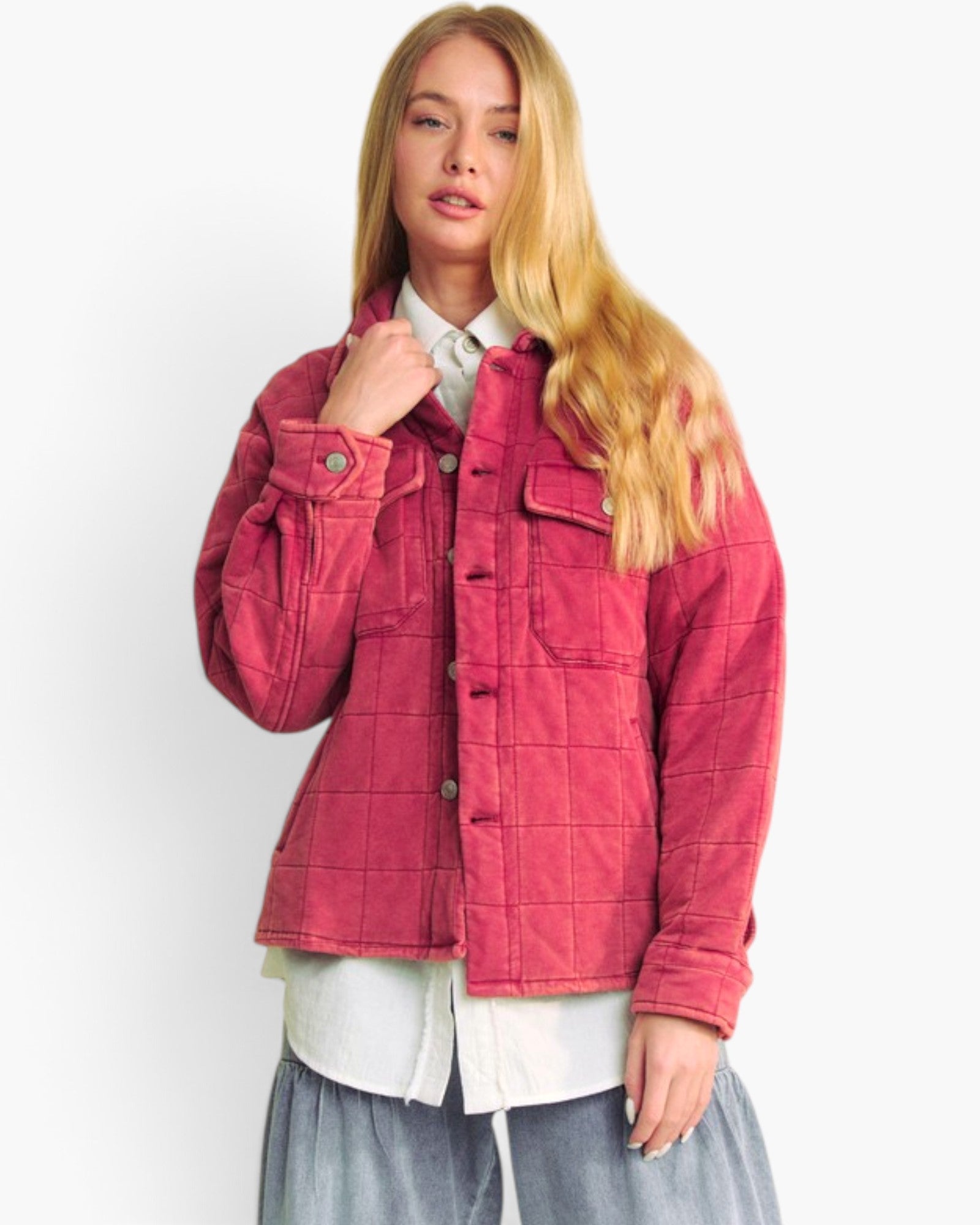 A blonde model wearing a pink quilted corduroy jacket over a white collared shirt and gray skirt, photographed against a plain white studio background.